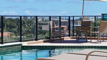 Área de piscina no terraço com vista para a cidade, uma mesa com cadeiras e um guarda-sol.