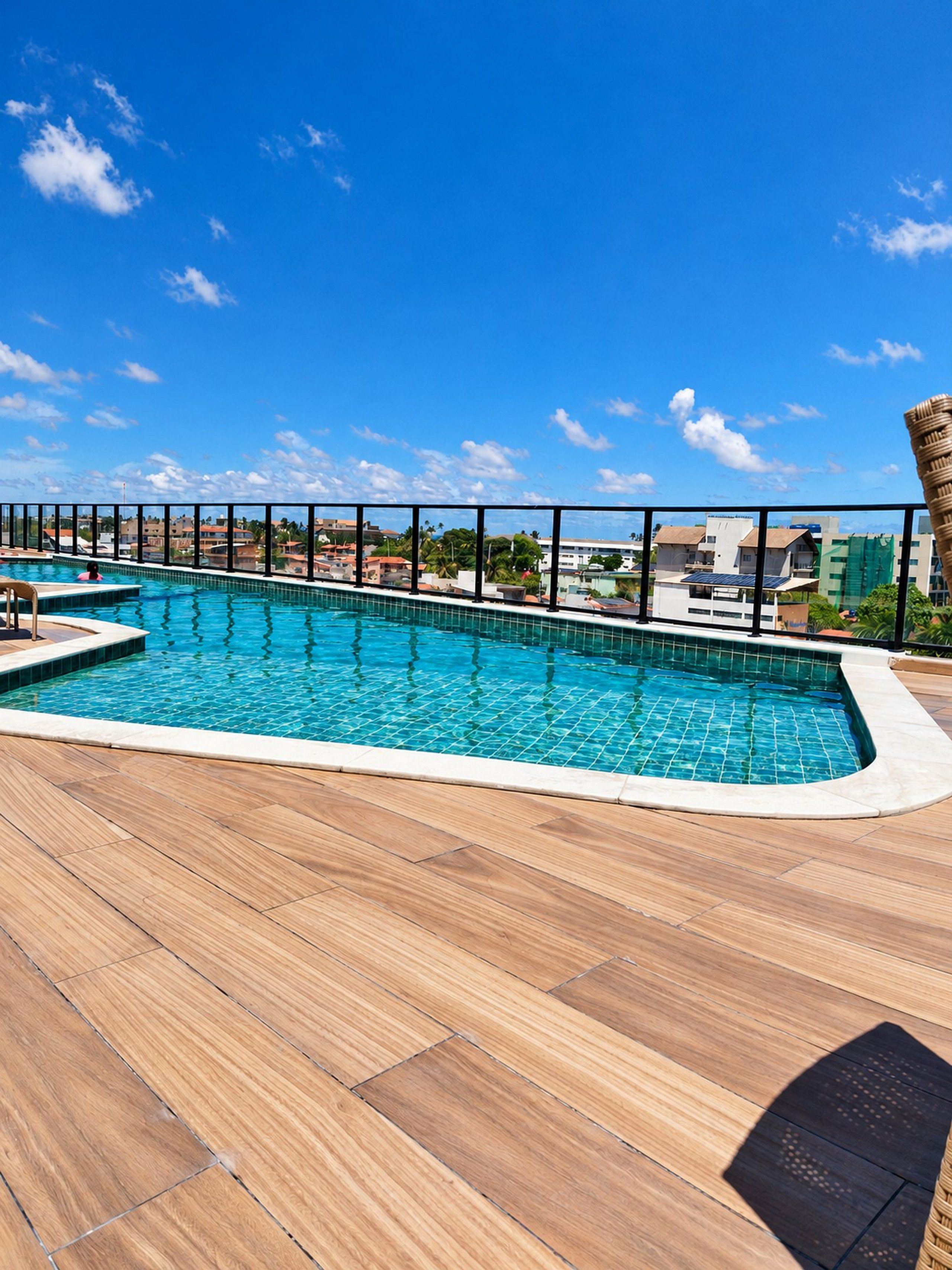 Une piscine avec une terrasse carrelée, entourée d’une rambarde en métal, et un ciel bleu clair en arrière-plan.