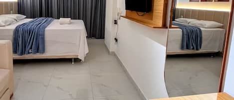 Ein Hotelzimmer mit zwei Betten, einem an der Wand befestigten Fernseher, einem Spiegel und einem Essbereich mit Tisch und Stühlen.
