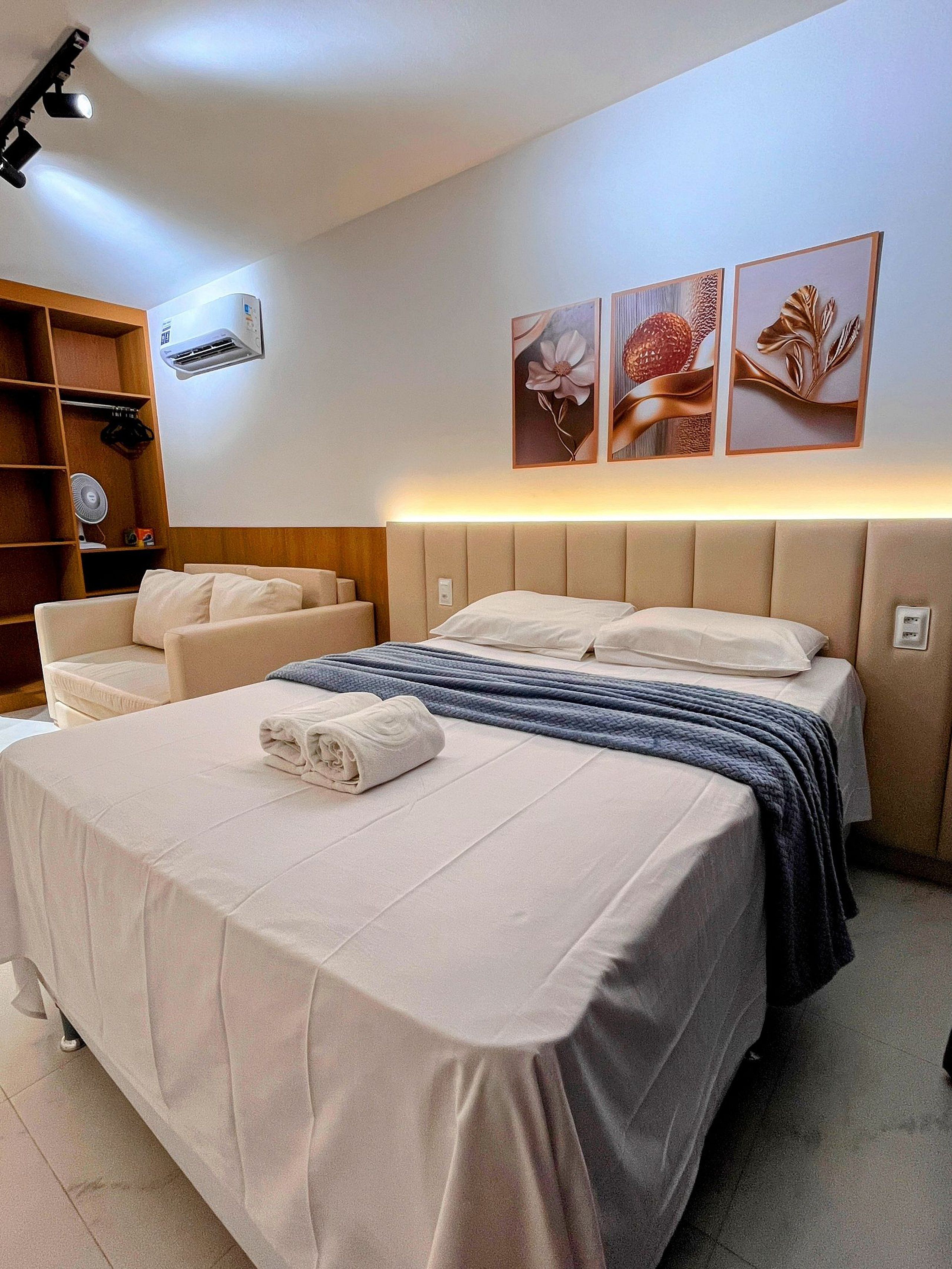 A hotel room with a bed, a sofa, a wardrobe, and wall-mounted artwork.