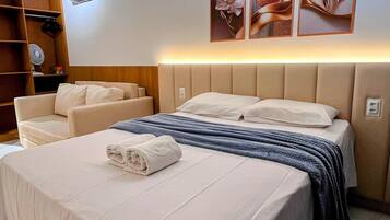 A hotel room with a bed, a sofa, a wardrobe, and wall-mounted artwork.