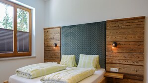 Un lit double avec une tête de lit en bois et deux tables de chevet, une fenêtre avec des stores et un mur orné d’un panneau texturé.