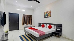 A modern bedroom with a bed, bedside tables, a ceiling fan, a door, and a painting on the wall. - Shree Ji Kunj (Udaipur)