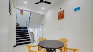 A dining area with a round table and four chairs, a ceiling fan, and a staircase in the background. - Shree Ji Kunj (Udaipur)