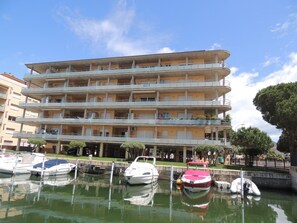Um edifício de vários andares com varandas, uma marina com barcos e um céu limpo.