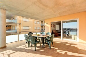 Uma área de refeições com uma mesa redonda e cadeiras, uma varanda com guarda-corpo e vista para um edifício sobre a água.