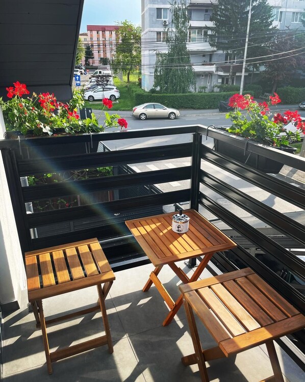 A balcony with two wooden tables and chairs, surrounded by potted plants with red flowers.