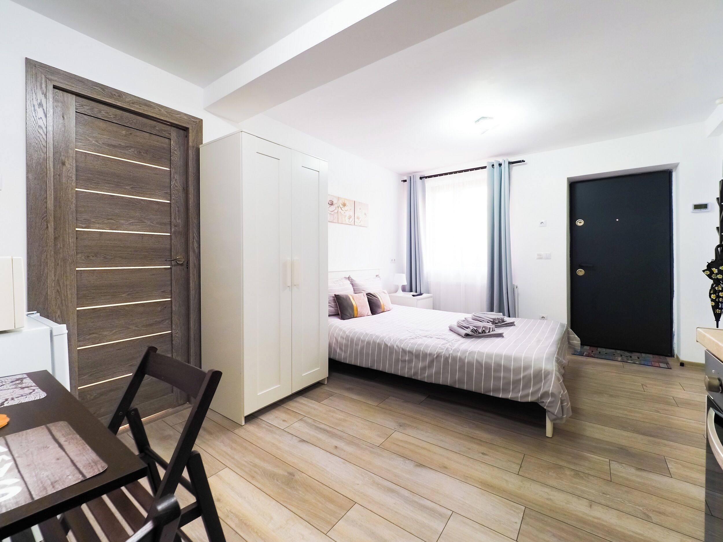 Una habitación pequeña con cama, armario, escritorio y silla, y una puerta.