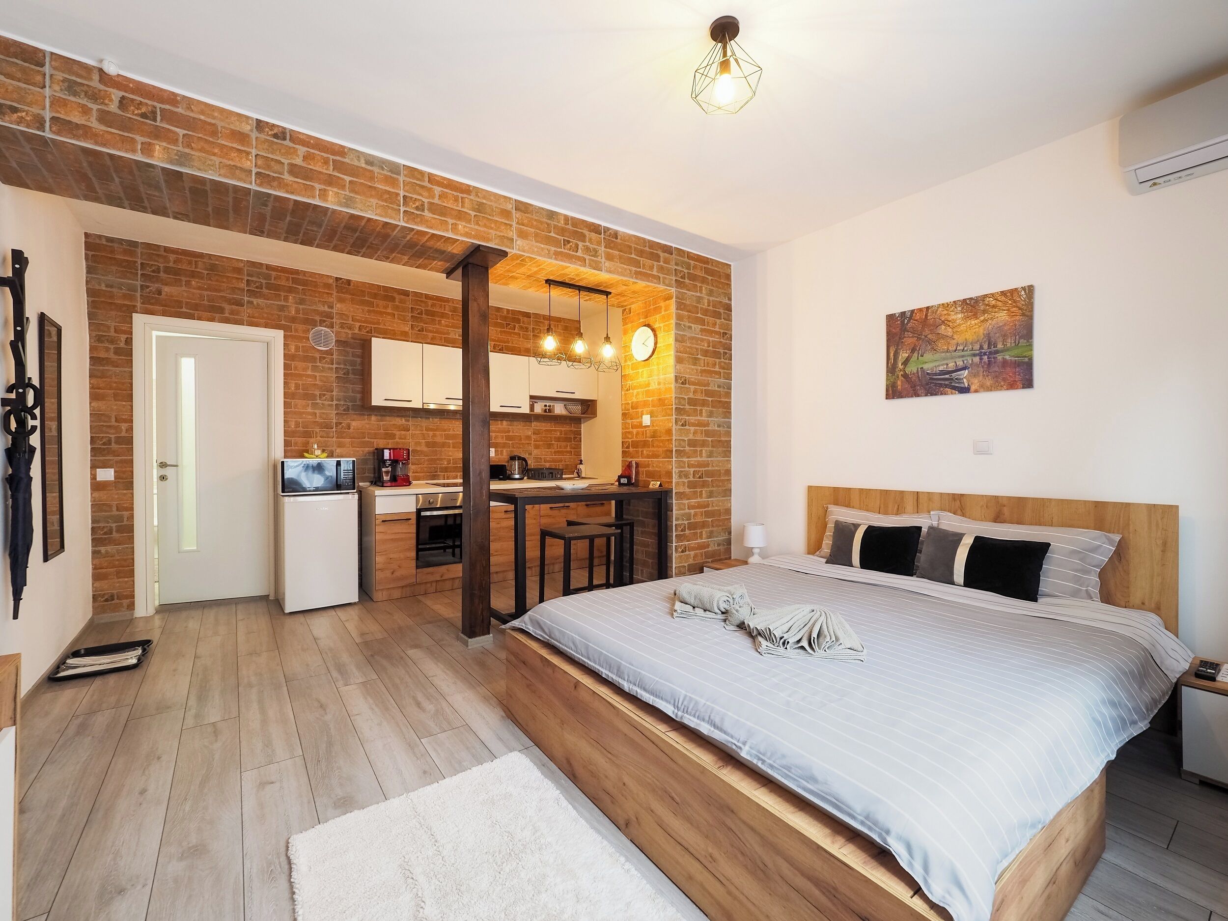 Un dormitorio moderno con una cama de madera, una pequeña kitchenette y una pared de ladrillo.