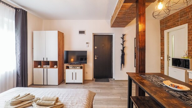 A modern hotel room with a bed, a TV, a wooden dining table, and a brick wall. - Ben Apartments (Sibiu)