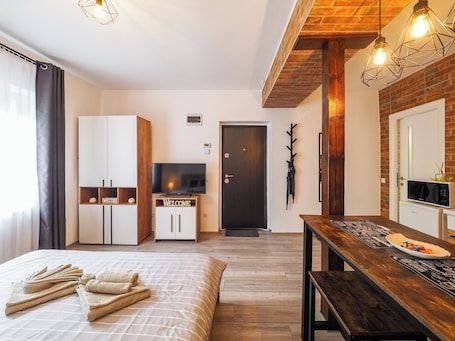 A modern hotel room with a bed, a TV, a wooden dining table, and a brick wall.