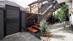 A modern outdoor staircase with a metal railing, a small garden area with a tree, and a patio table with chairs. - Ben Apartments (Sibiu)