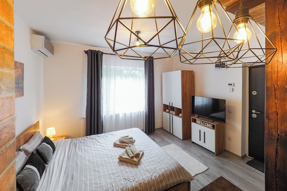 A modern hotel room with a bed, a TV, a wardrobe, and a unique geometric light fixture.