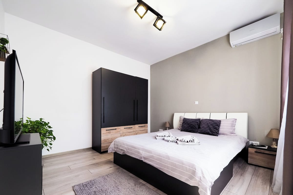 A modern bedroom with a bed, a wardrobe, a TV, and an air conditioner.