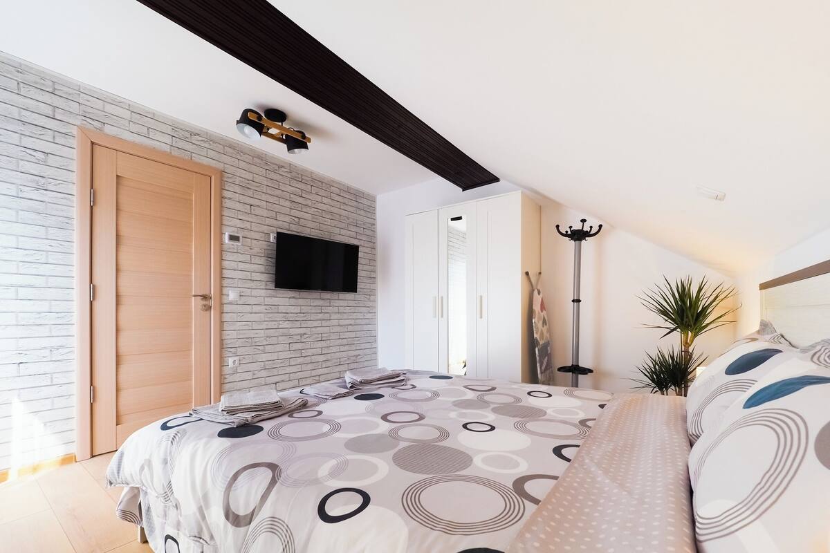 A bedroom with a bed, a TV mounted on the wall, a coat rack, and a plant.