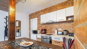 A modern kitchen with a brick backsplash, white cabinets, and a wooden dining table with a menu placemat. - Ben Apartments (Sibiu)