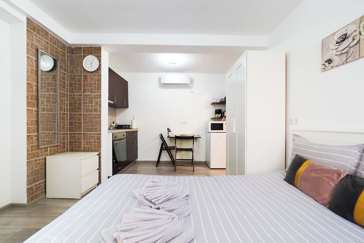 A compact hotel room with a bed, a small kitchenette, a dining area, and a bathroom.