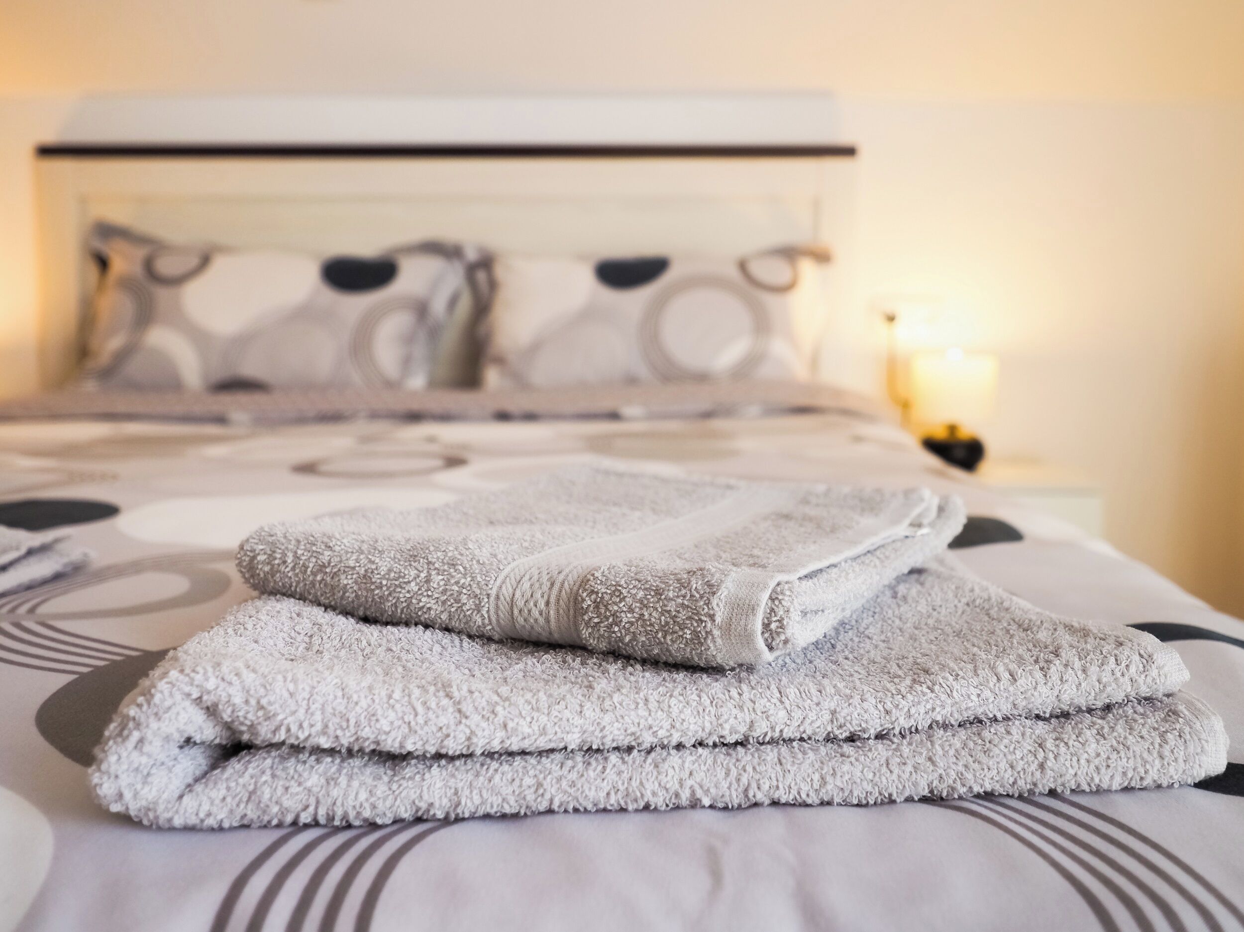 Un lit bien fait, avec une couvre-lit à motifs et des oreillers, et une pile de serviettes pliées posée sur le lit.