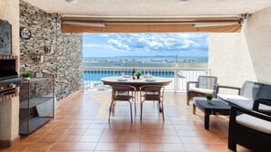 Une terrasse avec un mur en pierre, un barbecue, des meubles en osier et une vue sur la mer.