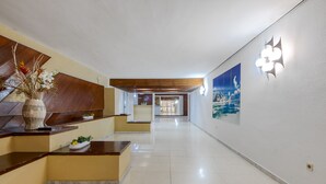Un espace d’accueil d’hôtel avec un comptoir de réception en bois, un vase rempli de fleurs et un luminaire fixé au mur.