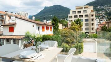 Un balcon avec une table dressée pour le dîner, offrant une vue sur un paysage montagneux et des immeubles résidentiels.