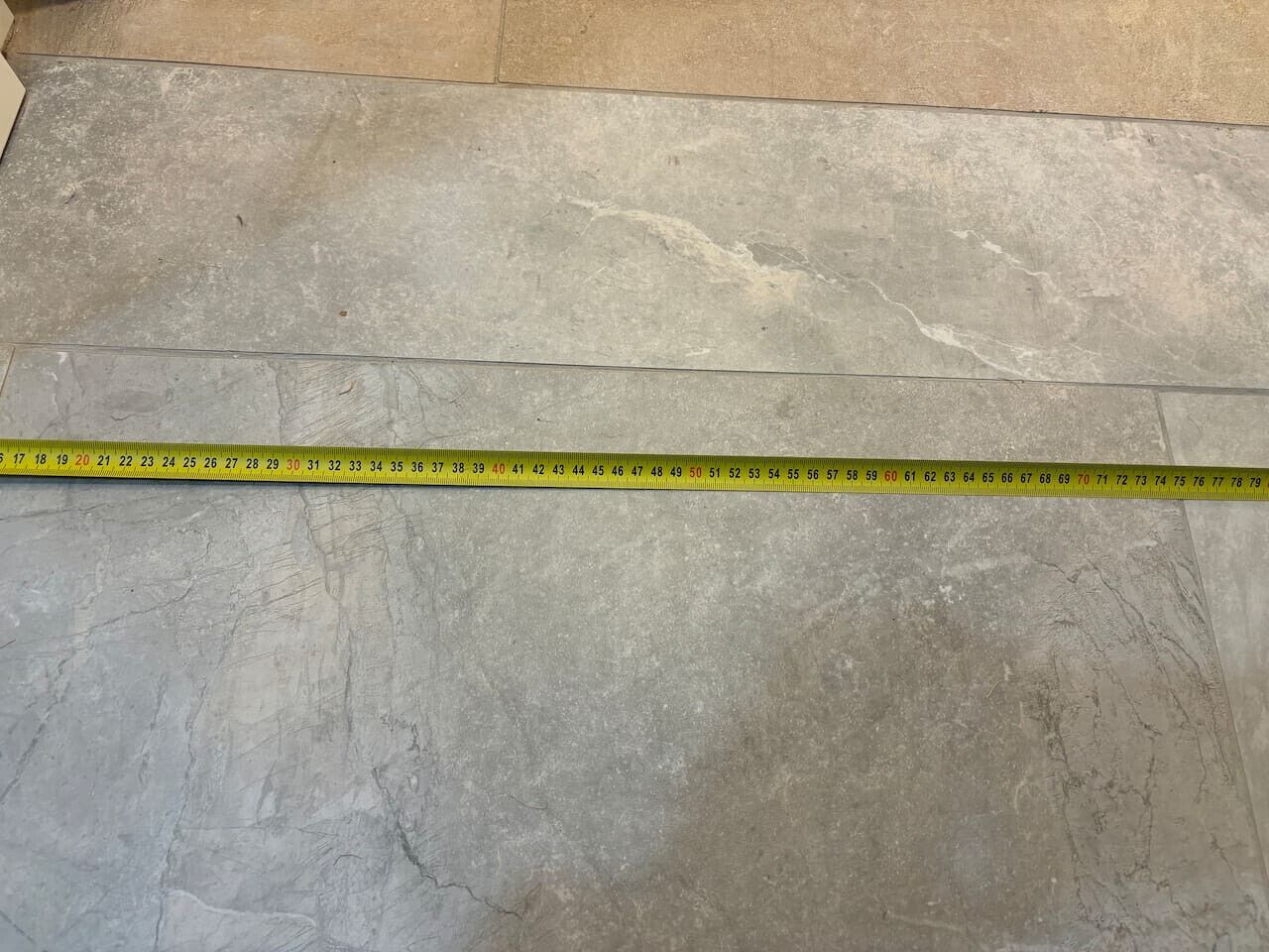 A measuring tape laid across a textured stone floor.