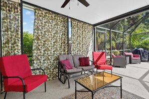 A sunlit patio area with a glass enclosure, red and grey furniture, and a tropical leaf-patterned wall. - New - 3 King Size Beds - Screened in Pool - Grill - 7 Minutes to Manasota Key! (Venice)