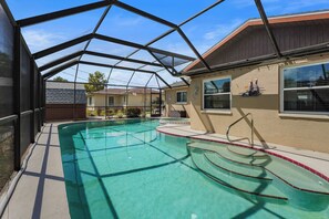 A swimming pool with a glass enclosure, surrounded by a fence, and adjacent to a building with a window and a wall-mounted bird feeder. - New - 3 King Size Beds - Screened in Pool - Grill - 7 Minutes to Manasota Key! (Venice)