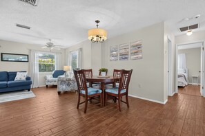 A living room with a blue sofa, a dining table with chairs, a ceiling fan, and a chandelier. - New - 3 King Size Beds - Screened in Pool - Grill - 7 Minutes to Manasota Key! (Venice)
