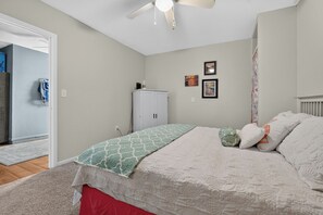 A bedroom with a bed, a ceiling fan, a wardrobe, and a door leading to another room.