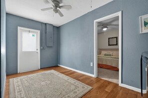 A room with a wooden floor, a patterned rug, a ceiling fan, and a door with a light switch. - New - 3 King Size Beds - Screened in Pool - Grill - 7 Minutes to Manasota Key! (Venice)