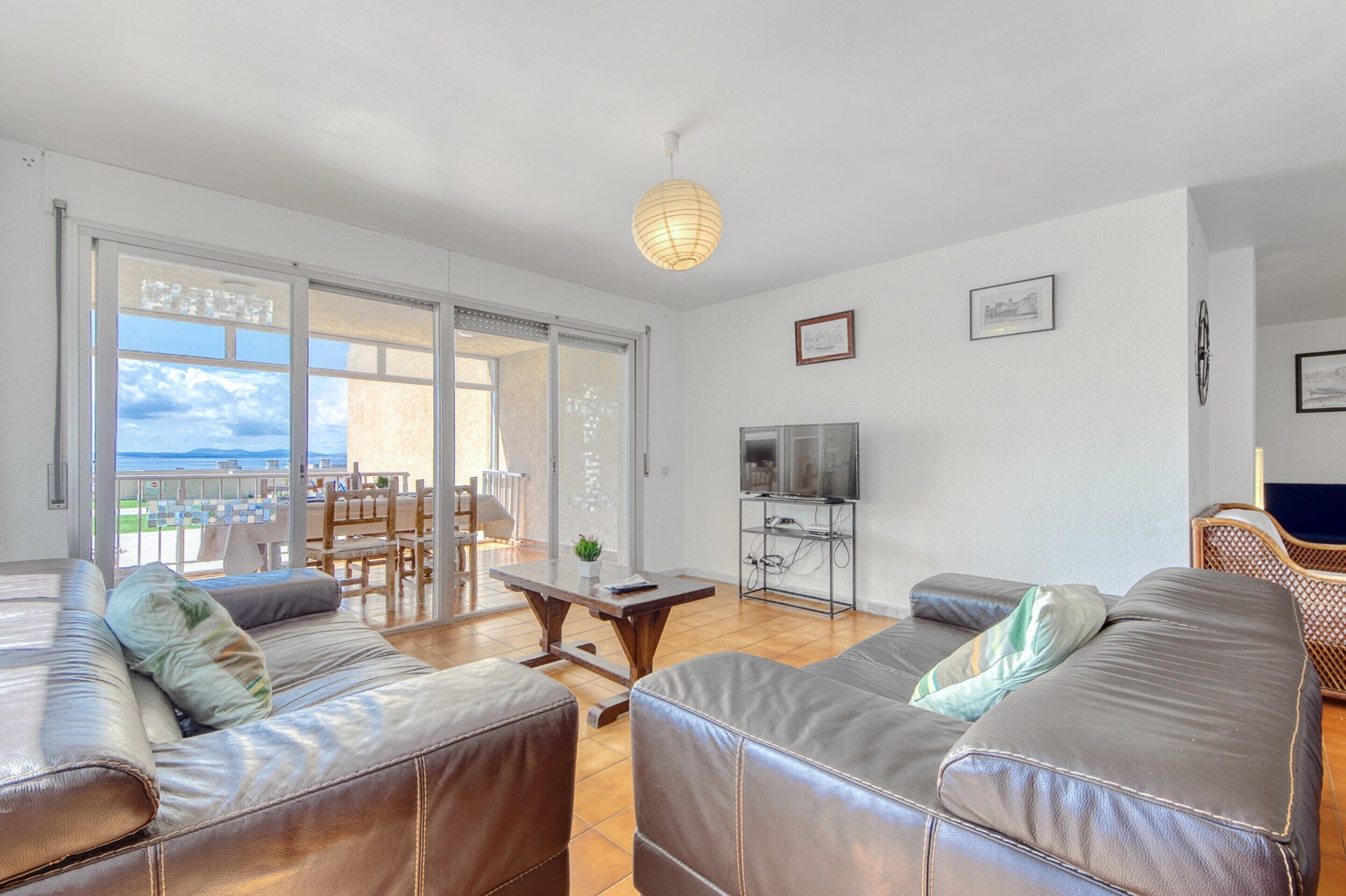 A spacious living room with leather sofas, a TV, and a balcony with a view.