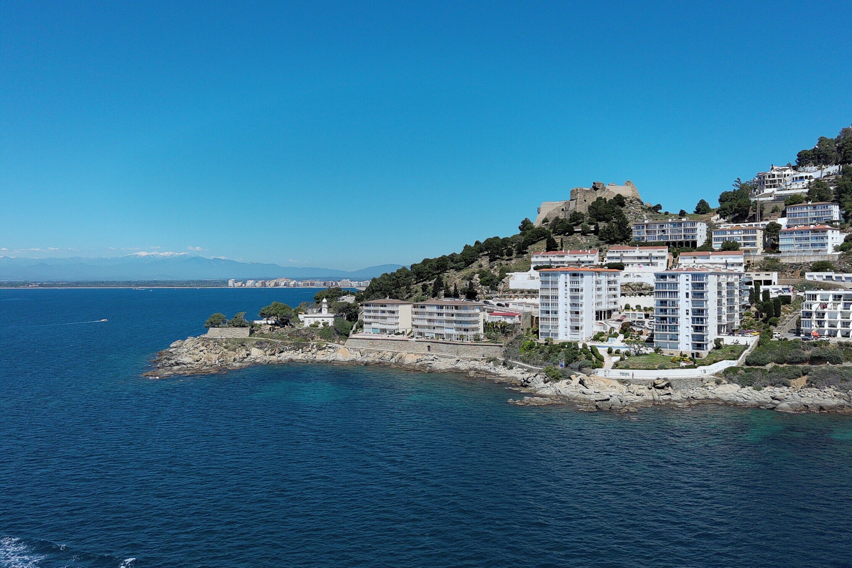 A coastal town with modern buildings, a historic fort, and a clear blue sea.