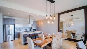 Une cuisine moderne dotée d’appareils électroménagers en acier inoxydable, d’une table à manger en bois avec des chaises et d’un éclairage suspendu.