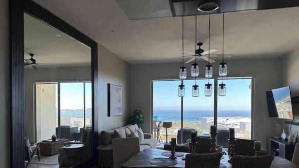 Un salon moderne avec un coin repas, de grandes fenêtres offrant une vue sur la ville et l’océan, et un ventilateur de plafond.