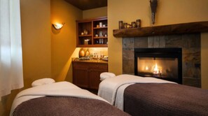 Two beds with white pillows and brown blankets, a cabinet with glass doors, and a stone fireplace create a warm and inviting space.
