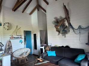 A room with a wooden ceiling, a clock, a sofa with blue cushions, a chair, and a wall with a decorative piece.