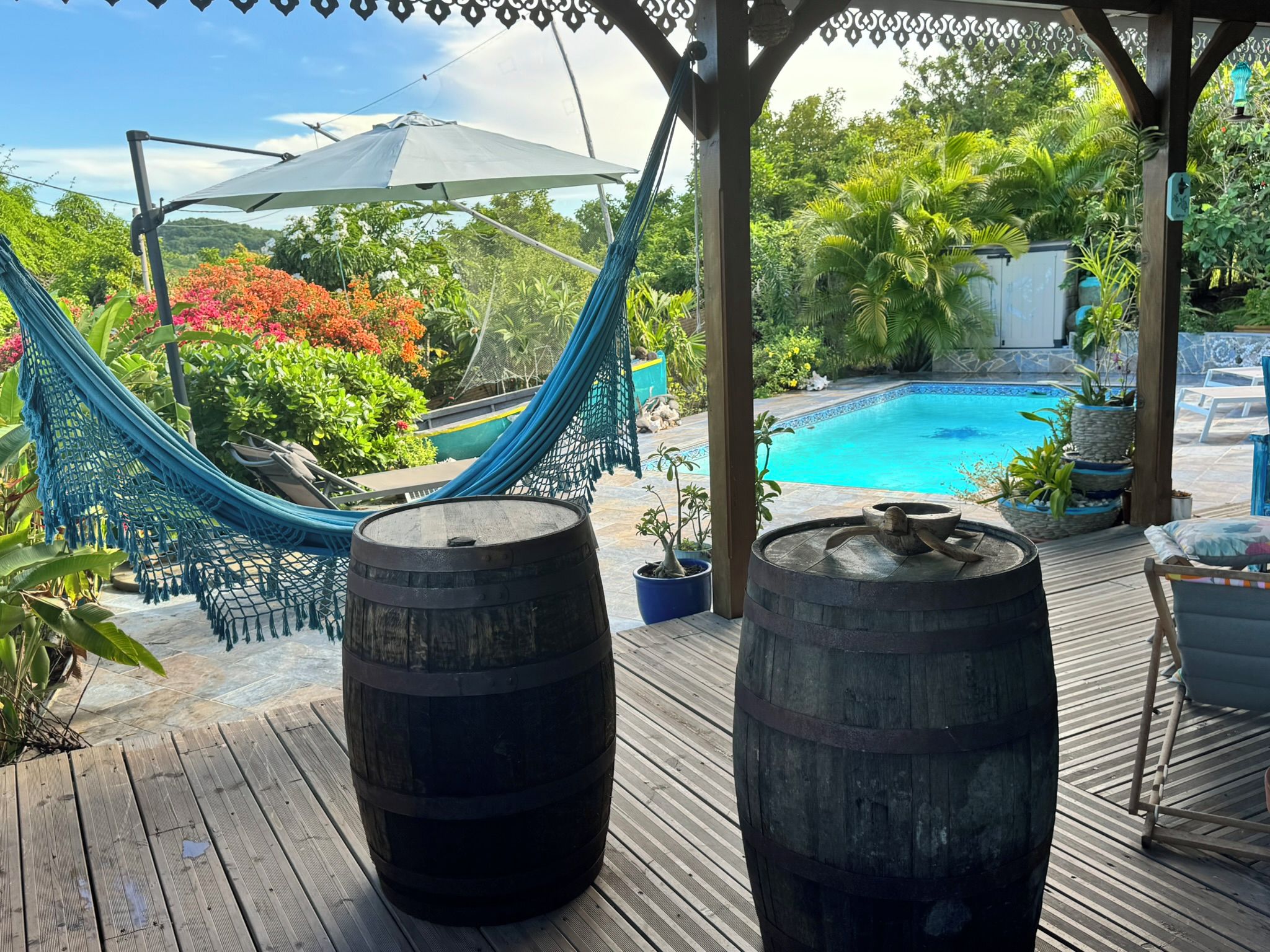 A wooden deck with a hammock, two barrels, and a pool.