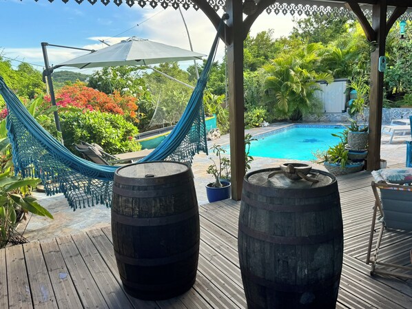A wooden deck with a hammock, two barrels, and a pool.