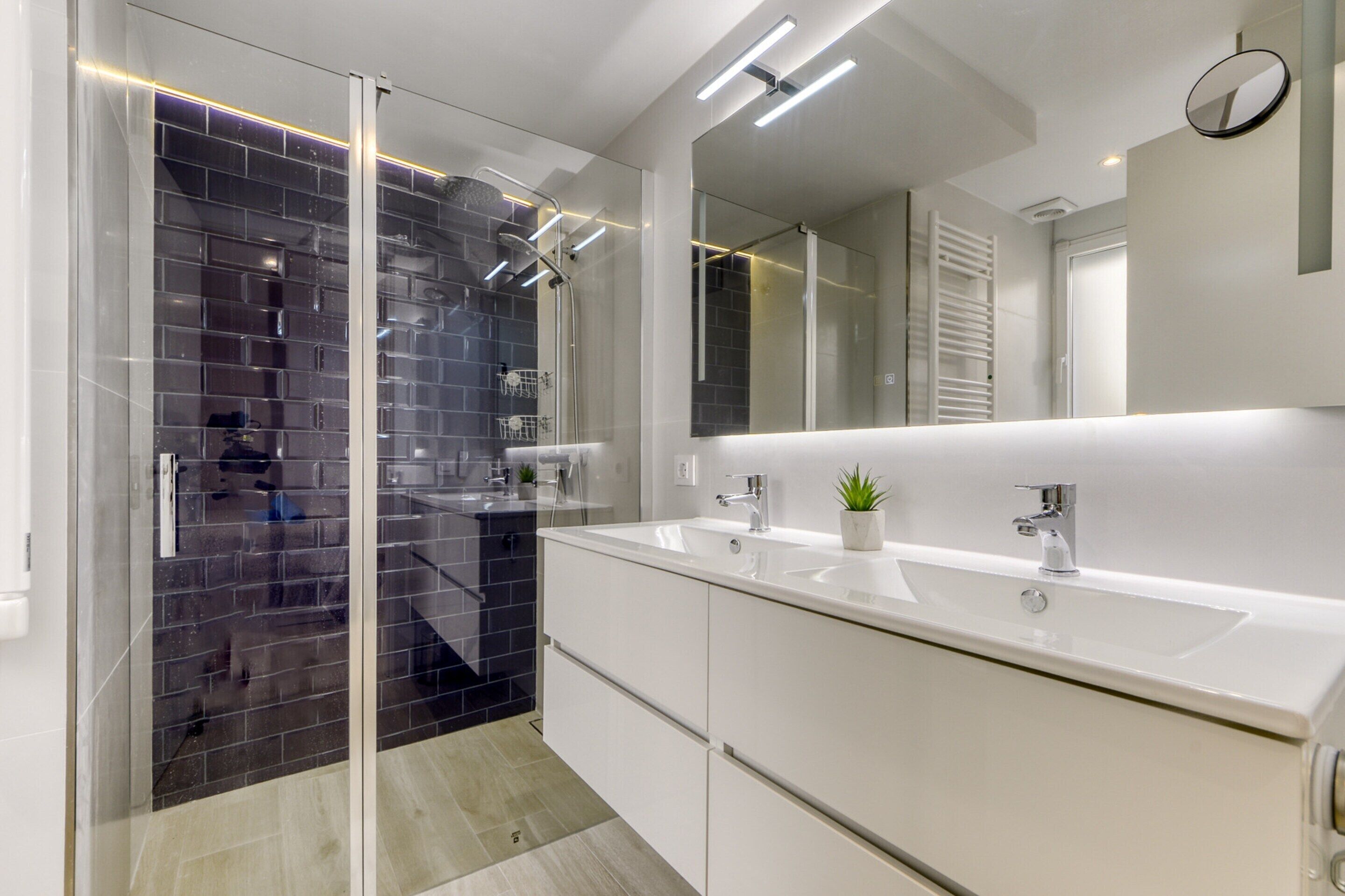 Un baño moderno con cabina de ducha de vidrio, tocador blanco con lavamanos y un espejo grande.