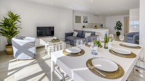 A modern living room with a dining area, a grey sofa, a flat-screen TV, and a potted plant. - Apartment in Roses Near Rock Beach (Roses)