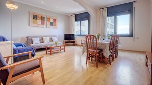 A living room with a sofa, a TV, a dining table with chairs, and artwork on the wall. - Beachfront Apartment With Terrace Views (Roses)