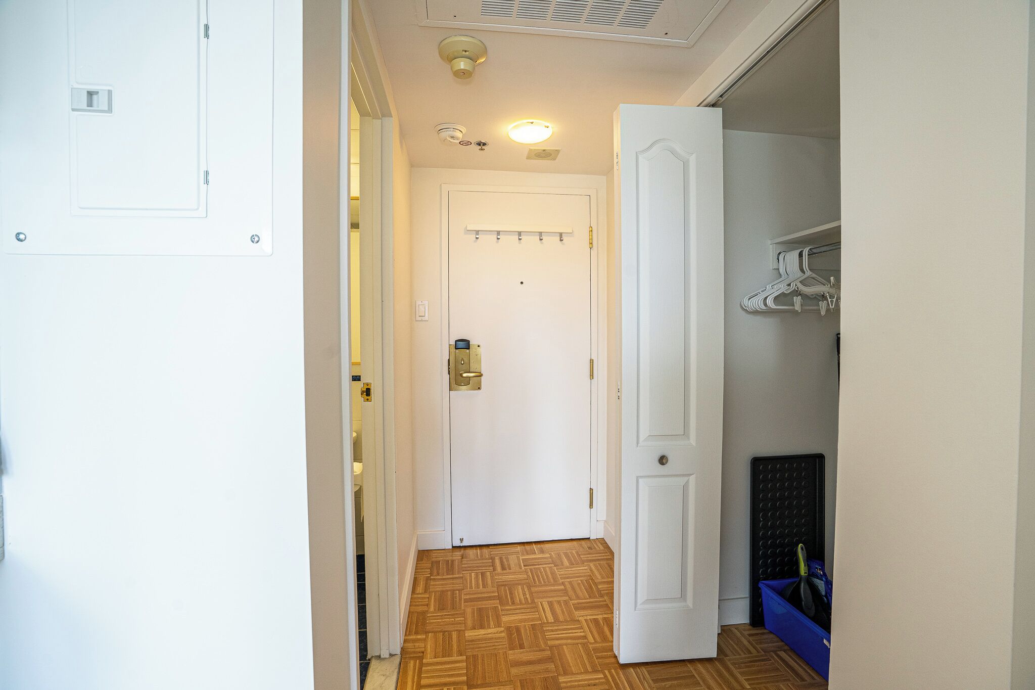 Un couloir avec un plancher en bois, une porte blanche avec une serrure et un porte-manteau avec des cintres.