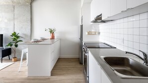 Moderni keittiö, jossa on valkoiset kaapit, keskellä oleva keittiösaareke, ruostumattomasta teräksestä valmistetut kodinkoneet ja betonikatto.
