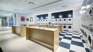 A modern laundromat with multiple washing machines, a wooden reception desk, and a checkered floor. - Modern Studio at Appartements Dorchester (Montreal)