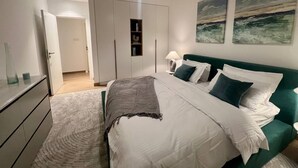 Un dormitorio con cama, mesita de noche, lámpara y una obra de arte en la pared.