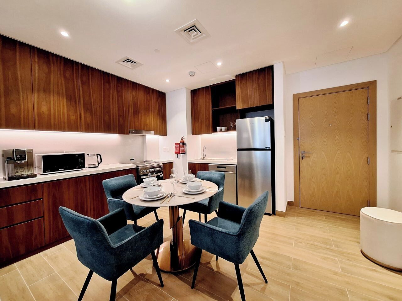 Eine moderne Küche mit Holzausstattung, einem Edelstahlkühlschrank und einem Essbereich mit blauen Stühlen und einem runden Tisch, gedeckt für vier Personen.