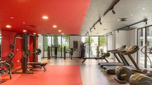 Un gimnasio con diverso equipo de ejercicio, ventanas amplias y suelo rojo.