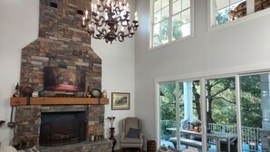 A cozy living room with a stone fireplace, a chandelier, and a view of the outdoors through large windows. - Private Equestrian estate in Aiken, SC. Only 30 miles to Augusta National.  (Aiken)
