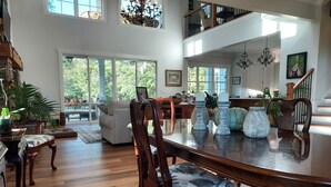 A spacious living room with a large wooden dining table, comfortable seating, and large windows offering a view of the outdoors. - Private Equestrian estate in Aiken, SC. Only 30 miles to Augusta National.  (Aiken)